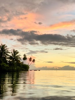 Sunset à Tahaa depuis l'eau avec vue sur les palmiers et un ciel plein de couleurs