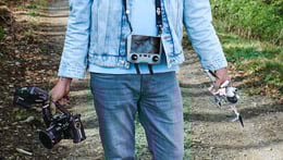 Mann in blauer Jeans und Jeansjacke, draußen, mit Kamera Rig und Drohne in den Händen, von vorne