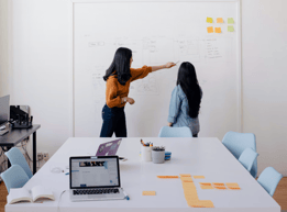 two women standing in front of a white board board