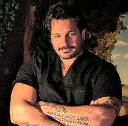 un homme brune bras croisé tatouage avec de la végétation 