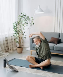 Hombre adulto mayor con barba blanca meditando con las manos en posición de oración frente a una laptop abierta sobre una est