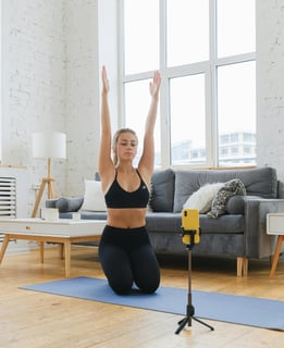Mujer joven sentada sobre un tapete de yoga en su sala de estar, estirando los br