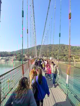 View of the iconic suspension bridge over the sacred Ganges River in Rishikesh, India, surrounded by lush greenery and hills.
