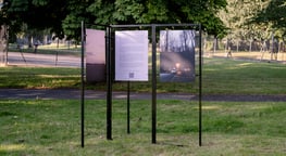 three photographs exhibited on black metal stands in a park