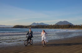 a bride and groom riding bicycles on the beach