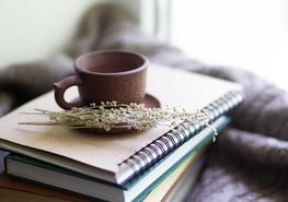 A photo of a purple mug sitting on a stack of brown books.