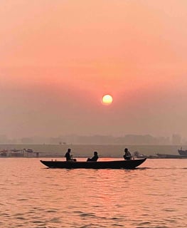 Sunrise over the Ganges River in Varanasi with a boat on the water.
