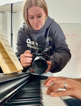 A young female filmmaker is filming a close-up of a piano players fingers as he plays a song.