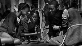 a group of young Black girls sitting on the ground playing jacks