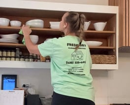 A professional cleaner thoroughly cleans a kitchen shelf with dishes