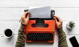 A writer typing on a typewriter, with a focus on the writing process and content creation.