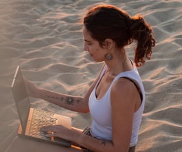 a woman sitting on a beach with a laptop