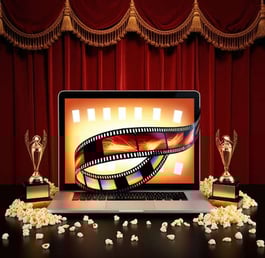 Film strip on a laptop screen with trophies and spilled popcorn on table