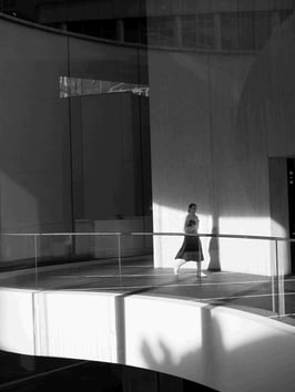 A woman walks on a mezzanine floor, silhouetted by sunlight.