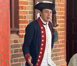 a man in a colonial era uniform standing in front of a brick wall