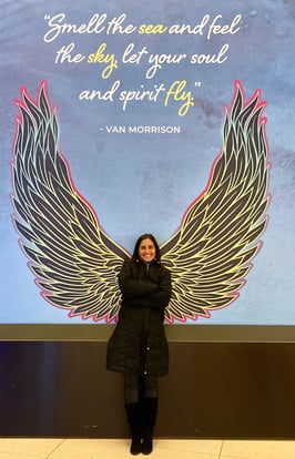 a woman standing in front of a large poster with angel wings and Van Morrison quote "Smell the sea"