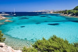 Aerial view of Costa Smeralda’s turquoise waters with luxury yachts anchored near a pristine beach.