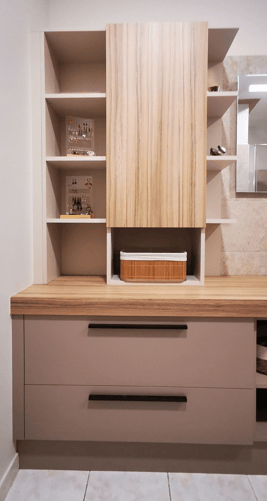 Salle de bains avec plan en bois clair veiné, meuble rosé, poignée métal. Miroir lumineux.