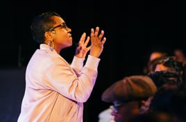 a Black woman in a pink jacket and glasses among audience