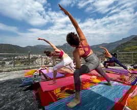 Person practicing yoga asanas outdoors with a scenic view of the Himalayan mountains in the background.