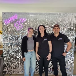 Laura and SweetAz crew in front of the silver shimmer wall and happy 18th neon after relocating.