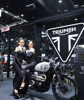 a woman standing next to a motorcycle with a woman sitting on it