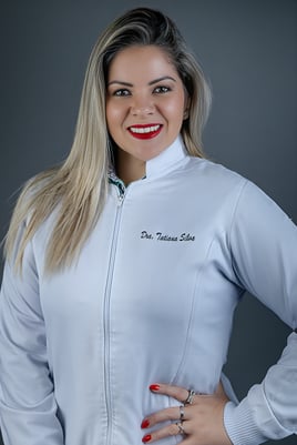 mulher loira dentista posando de jaleco em estúdio com fundo cinza enquanto sorri com batom vermelho