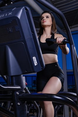 mulher olhando pra cima na academia enquanto sobe degraus no aparelho usando conjunto fitness