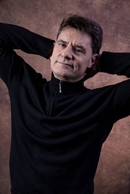 ator vestindo camisa preta em pose despojada cruzando os braços em ensaio fotográfico