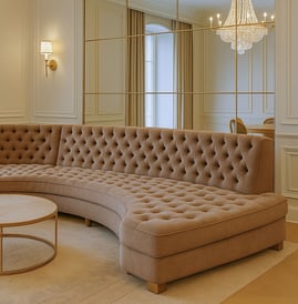 Luxurious curved tufted sofa in a transitional living room with chandelier, mirror, and soft lighting.