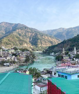 Scenic rooftop view overlooking the mountains and the cityscape of Rishikesh, India, under a clear sky.