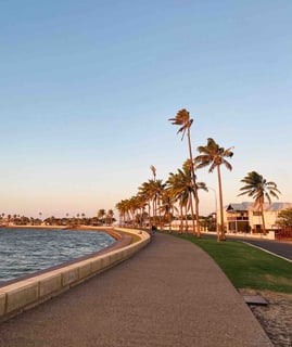 Peaceful walk between the water and coconut trees at sunset in Carnarvon, Western Australia.