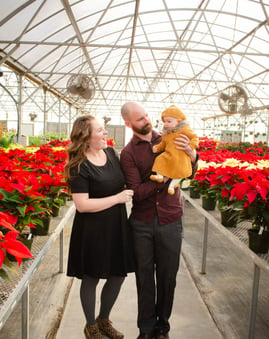 a man and woman holding a baby in a greenhouse