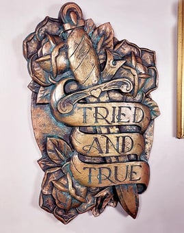 A plaque in the style of traditional tattoo art. Dagger with roses and a banner saying Tried & True