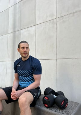 A personal trainer sat with dumbbells at his side