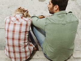 Una pareja hombre y mujer, sentados en el suelo, después de discutir