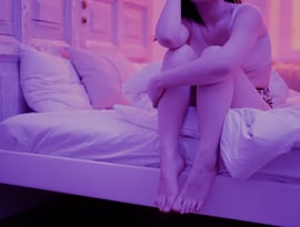 Mujer sentada en la cama, en habitación con tonalidades moradas