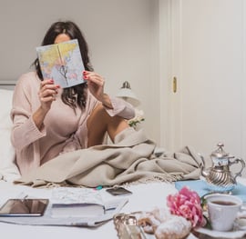 a woman sitting on a bed with a book and a cup of coffee