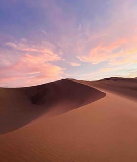 A beautiful sunset over the sand dunes of Huacachina desert in Peru, with bright orange and pink colors filling the sky.