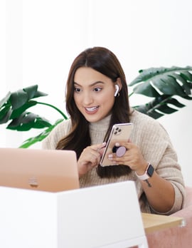 a woman sitting at a table with a cell phone and a laptop
