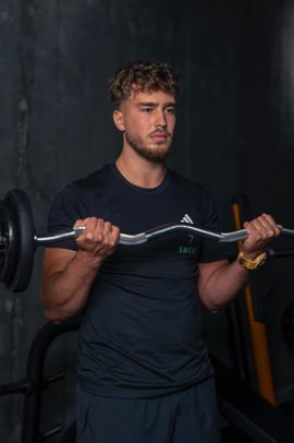 Antrenor personal executând flexii pentru biceps cu o bară EZ, într-o sală de fitness