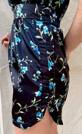 The side slit of a black satin cocktail dress with blue printed flowers