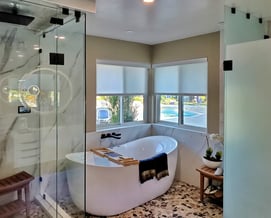 Elegant and bright master bathroom with marble wall, freestanding tub, and glass shower and toilet enclosures.