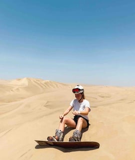 Manon sitting in the sand, ready to ride down the dunes of Huacachina on a sandboard, in the Peruvian desert.