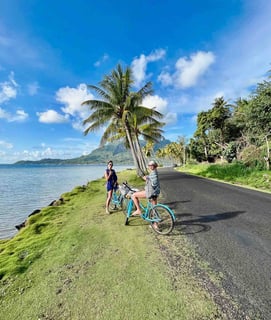 Eva and Manon cycling on a palm-lined road in Bora Bora, French Polynesia.