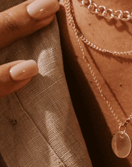 a woman wearing a tan jacket and a gold chain necklace