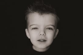 4-year-old boy squints curiously into the camera during a personality portrait session on a black ba