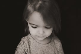 Two-year-old girl looking down thoughtfully against a black backdrop during a personality portrait s
