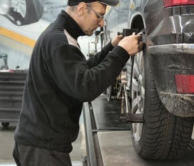 a man in a black jacket is aligning a frame of a car at fix collision center