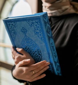 femme serrant un coran bleu contre elle refflètant l'amour de l'apprentissage du coran
